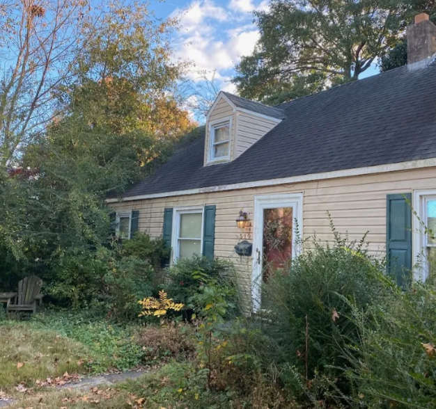 The front of a beat up house with over grown bushes