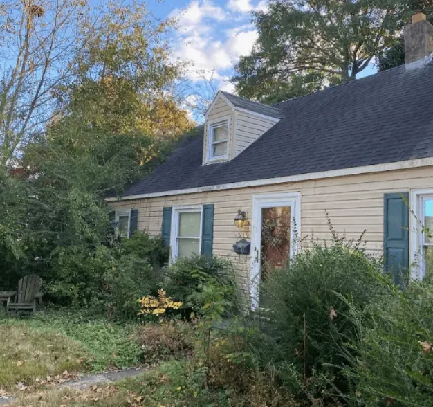The front of a beat up house with over grown bushes